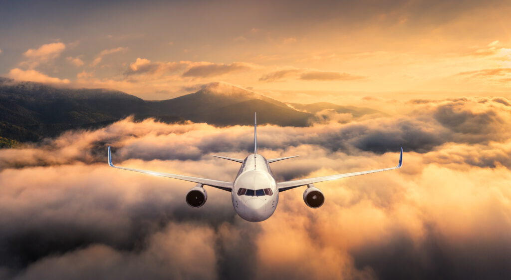 Airplane is flying above the clouds at sunset in summer. Landscape with passenger airplane, mountains, orange sky. Aircraft is taking off. Business travel. Commercial plane. Aerial view. Transport. An example of fiber-reinforced thermoplastics in aerospace